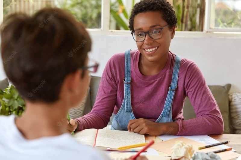 Team work process. back view of groupmates have discussion over notepad and documents, sit at work place, have happy expression. positive afro american female pose in coworking space with trainee Free Photo