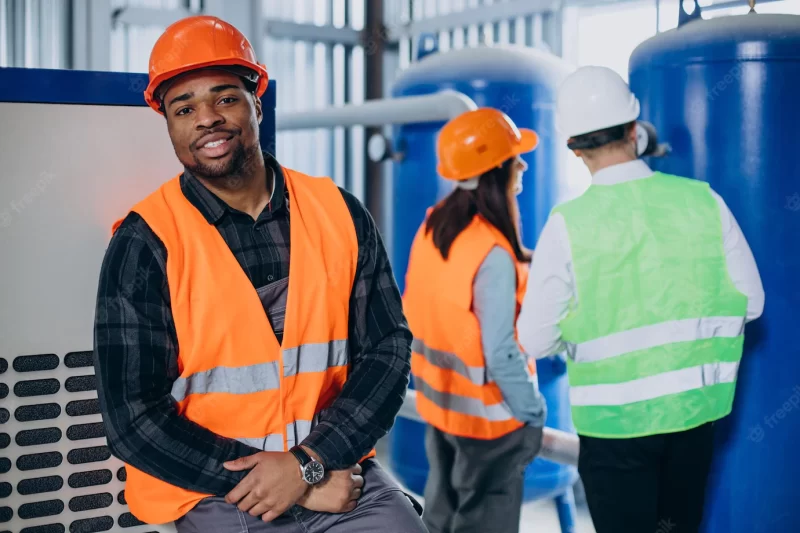 Three factory workers in safety hats discussing manufacture plan Free Photo