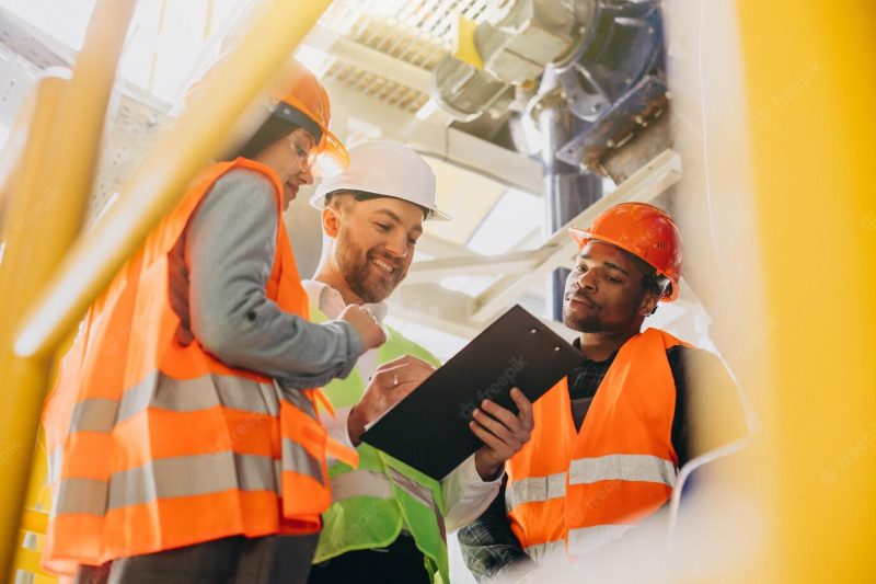 Three people discussing a plan at a factory Free Photo