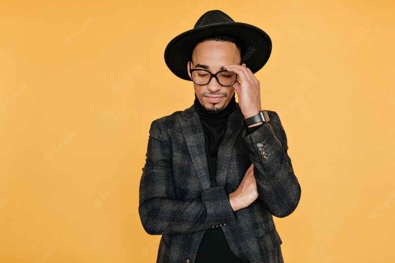 Tired black young man in formal attire posing with eyes closed. photo of african guy in trendy casual clothes standing on yellow wall. Free Photo