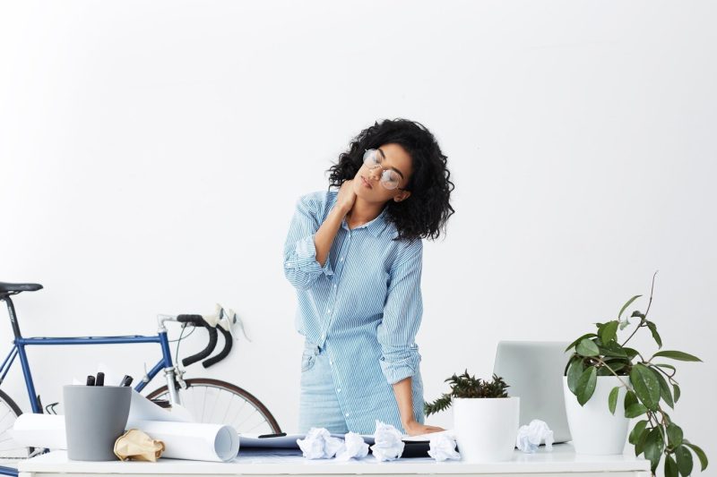 Tired cute African girl with closed eyes standing at her workplace covered with documents Free Photo