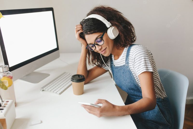 Tired pretty young woman sitting at workplace propping head and texting message, holding phone Free Photo