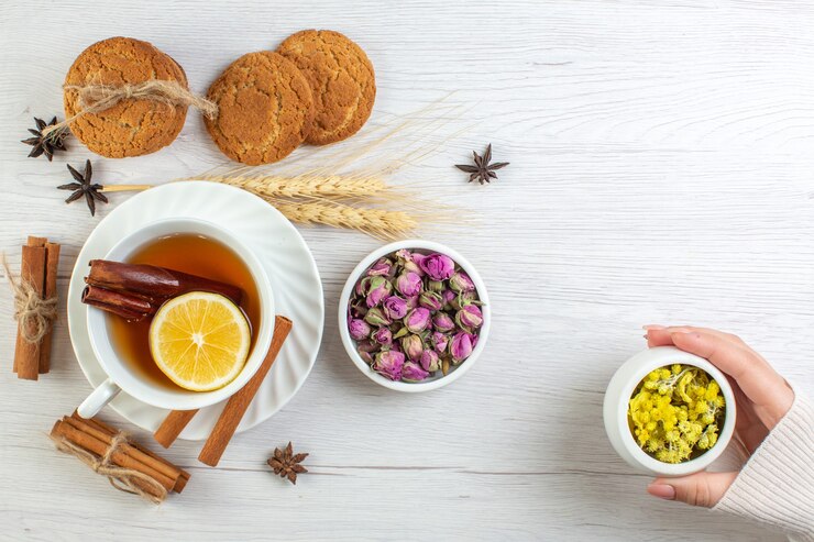 Top View Woman Hand Holding Herbal Pot With Black Tea With Cinnamon Lime Lemon Various Herbals Cookies White Background 140725 130674