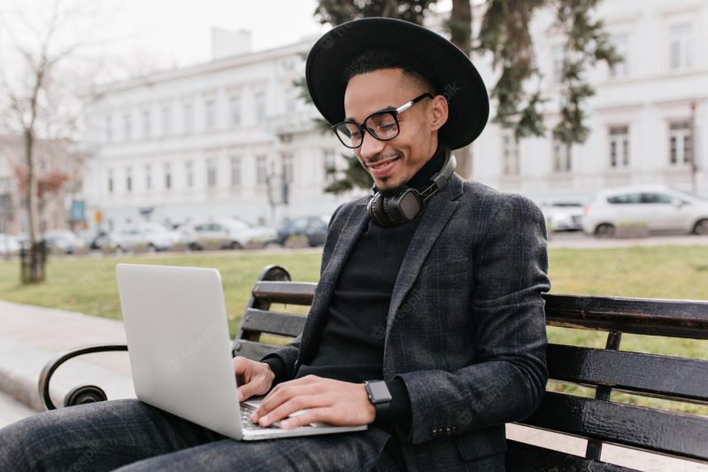 Trendy international student working with laptop in park. smiling african man chilling outdoor with computer. Free Photo