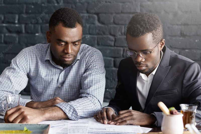 Two African American colleagues in formal wear sitting at desk with papers while working on financial report Free Photo