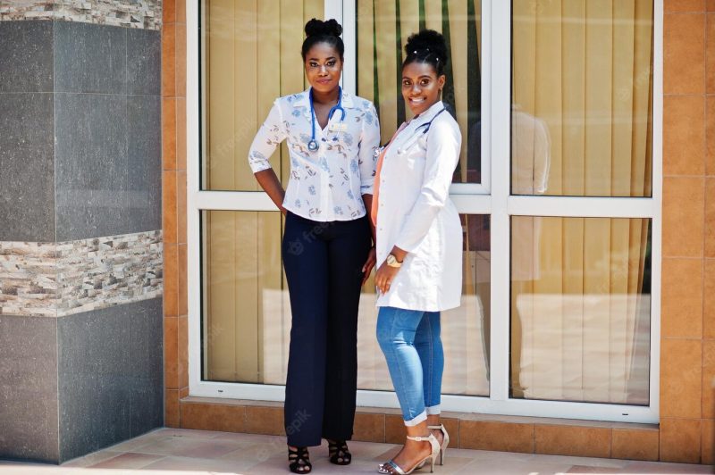 Two african american doctors female at lab coat with stethoscope posed outdoor against clinic Free Photo