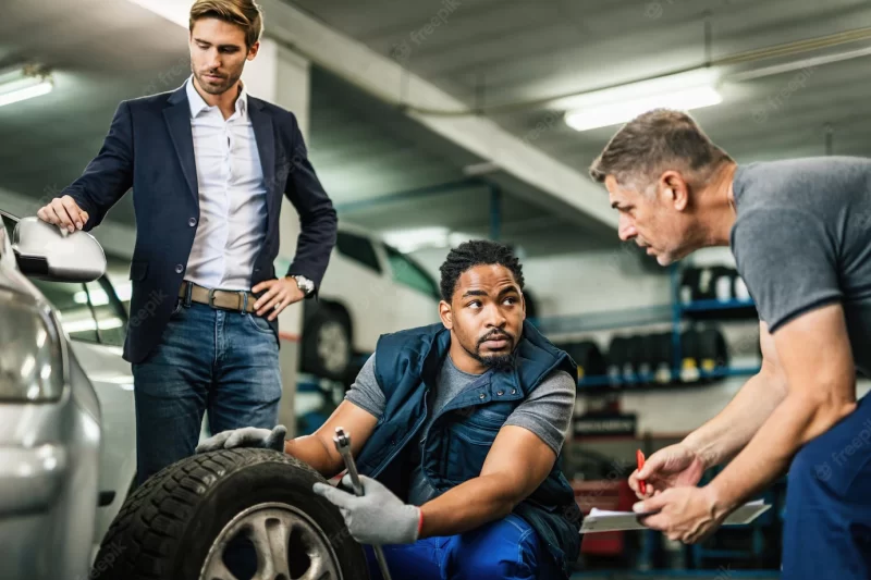 Two auto mechanics cooperating while repairing tire of customer’s car at auto repair shop Free Photo