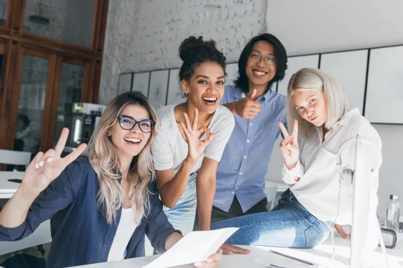 Two blonde female office workers posing with peace sign while fooling around with foreign colleagues Free Photo