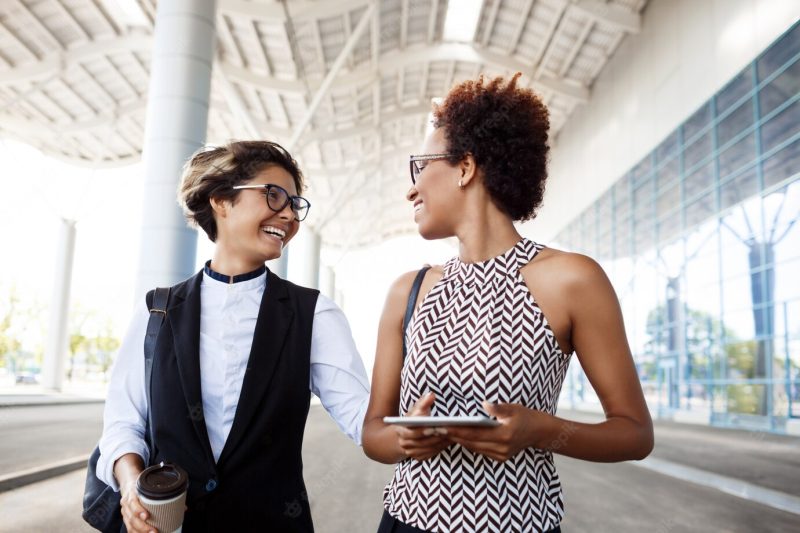 Two young successful businesswomen laughing, smiling over business centre. Free Photo