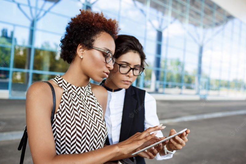 Two young successful businesswomen looking at tablet over business centre. Free Photo