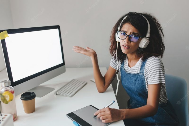 Unhappy black woman in denim overall pointing at computer screen complains about bad internet Free Photo