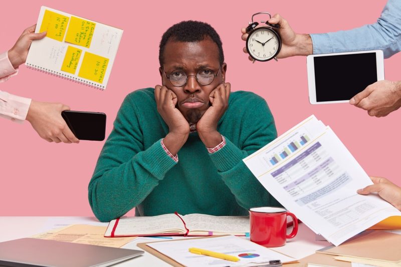 Upset black male worker has much work, thinks about business project, being lack of time Free Photo