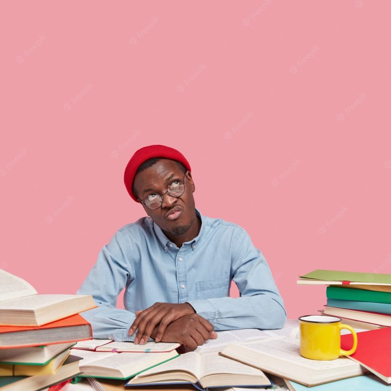 Vertical image of sad thoughtful african american man dressed in stylish clothing, concentrated upwards, wears spectacles Free Photo