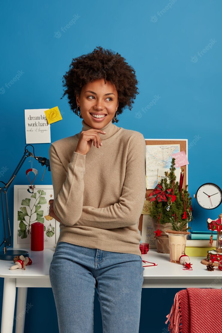 Vertical Shot Cheerful Satisfied Afro American Female Student Stands Near Workplace Against Blue Wall Keeps Hand Chin Looks Away Thinks About Future Plans Pleased Work From Home 273609 37651