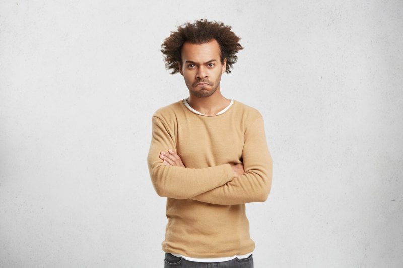 Waist up portrait of sullen grumpy man with bristle and curly hair, keeps arms folded Free Photo