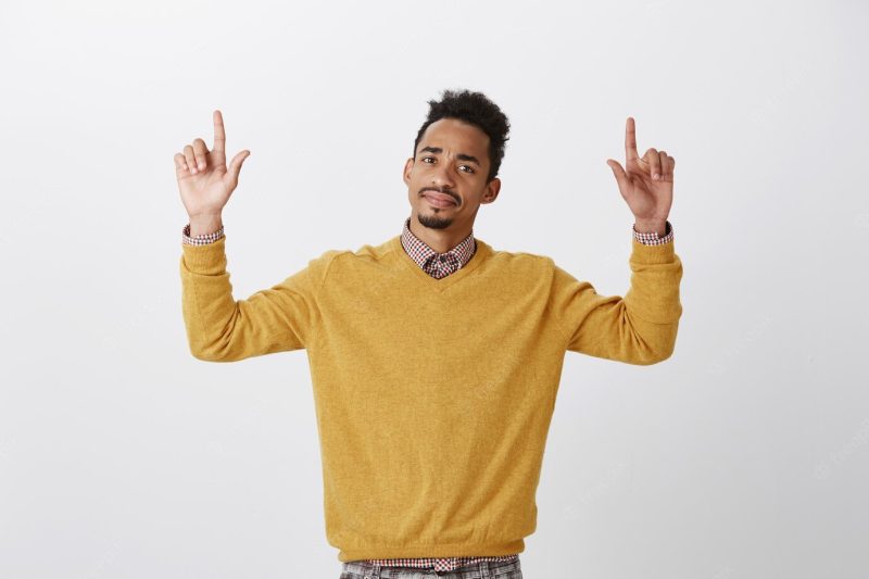 What a disappointment. portrait of displeased doubtful American guy with Afro hairstyle raising hands and pointing up with index fingers, expressing disgust and doubt, standing Free Photo