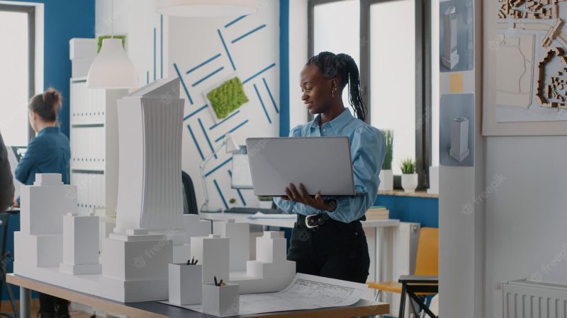 Woman architect holding laptop to analyze building model in architectural office. engineer working with computer and maquette to design construction structure for urban project. Free Photo