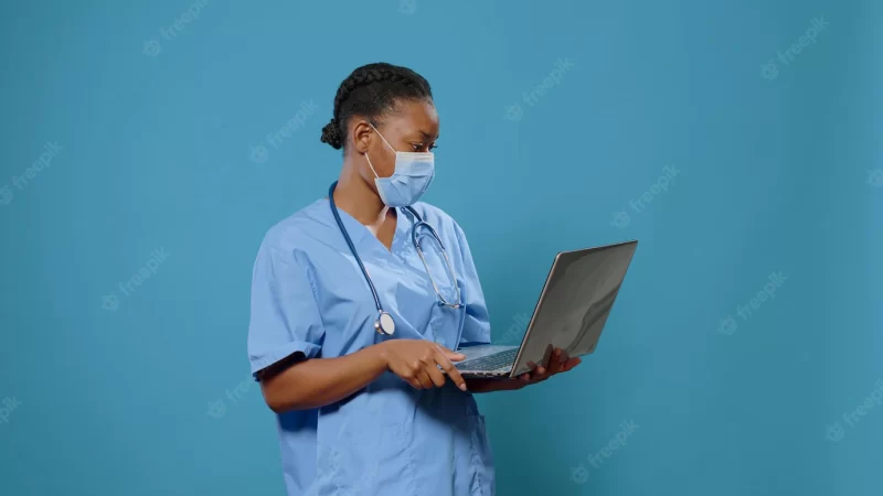 Woman nurse wearing face mask and using laptop in front of camera. medical assistant in uniform having protection against coronavirus while holding computer to work on healthcare. Free Photo