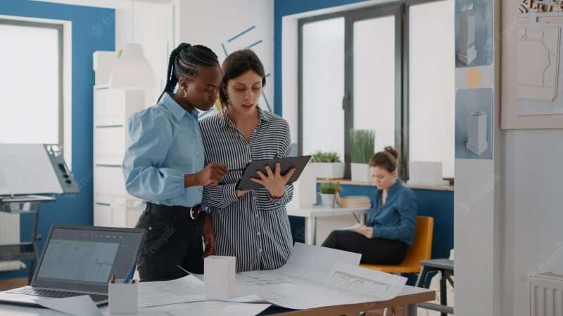 Women looking at digital tablet and blueprints to plan building layout for construction. colleagues working together to design structure and architectural development. architects at work Free Photo