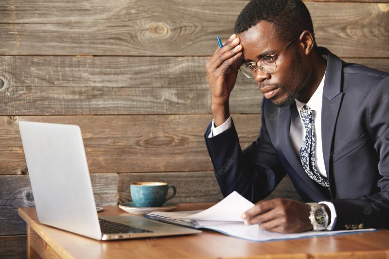 Worried African businessman in official suit checking information in laptop Free Photo