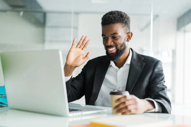 Young african american manager with stubble sitting in front of open laptop wearing earphones while having video conference call with business partners Free Photo