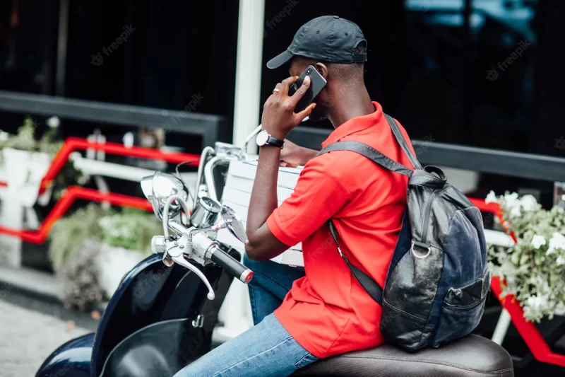 Young african guy accepts the order by phone and write in motorbike holding boxes with pizza Free Photo