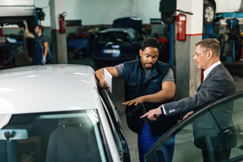 Young black auto mechanic and manager discussing about car breakdown in repair workshop Free Photo