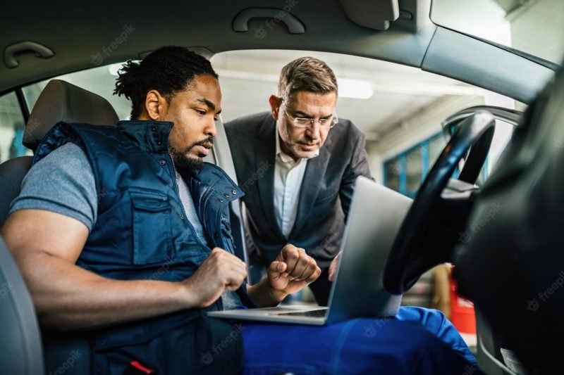 Young black car mechanic using computer with his manager in auto repair shop Free Photo