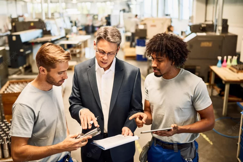 Young metal workers cooperating with their manager while reading reports in industrial building Free Photo