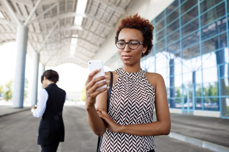 Young successful African businesswoman looking at phone over business centre. Free Photo