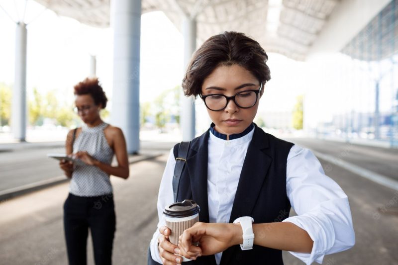 Young successful businesswoman looking at watch, standing near business centre. Free Photo