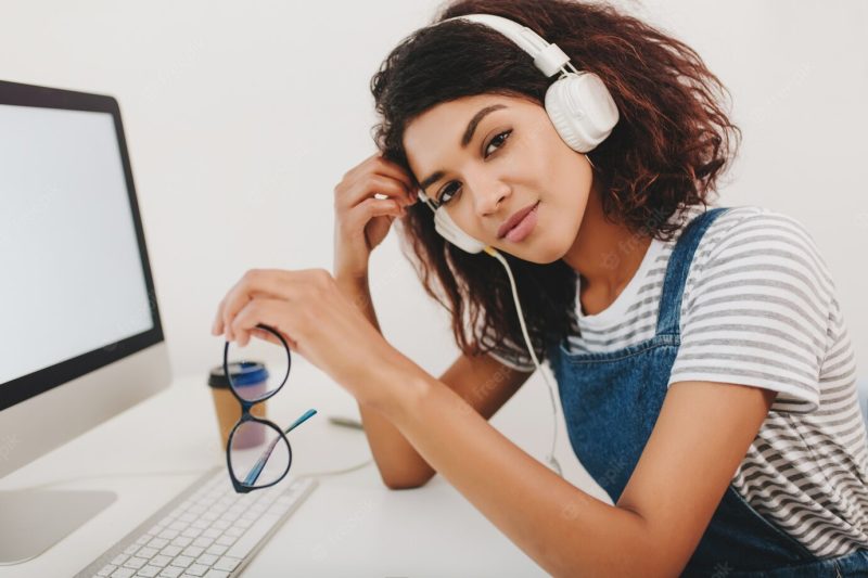 Young woman in stiped shirt with light-brown skin and big dark eyes posing while working with computer Free Photo