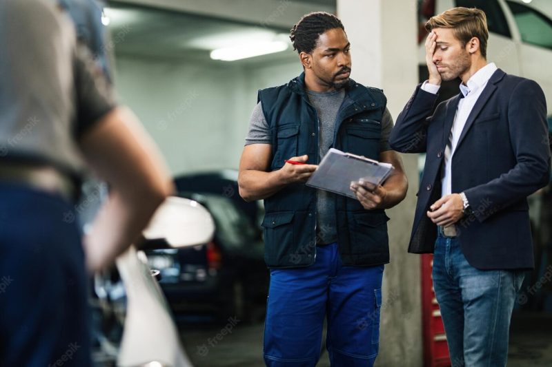 Young worried businessman talking with african american auto mechanic about costs of car reparation in auto repair shop Free Photo