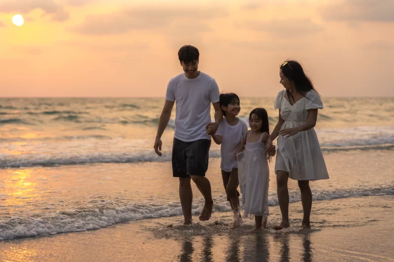 Asian young happy family enjoy vacation on beach in evening. dad, mom and kid relax walking together near sea when sunset while travel holiday trip. lifestyle travel holiday vacation summer concept. Free Photo