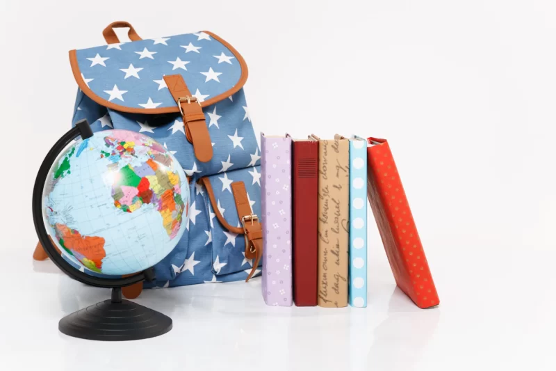 Close up of globe, blue backpack with stars print and colorful school books Free Photo
