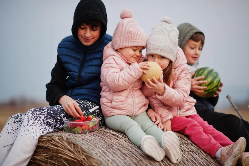 Four kids with fruits in hands sitting on haycock at field Free Photo