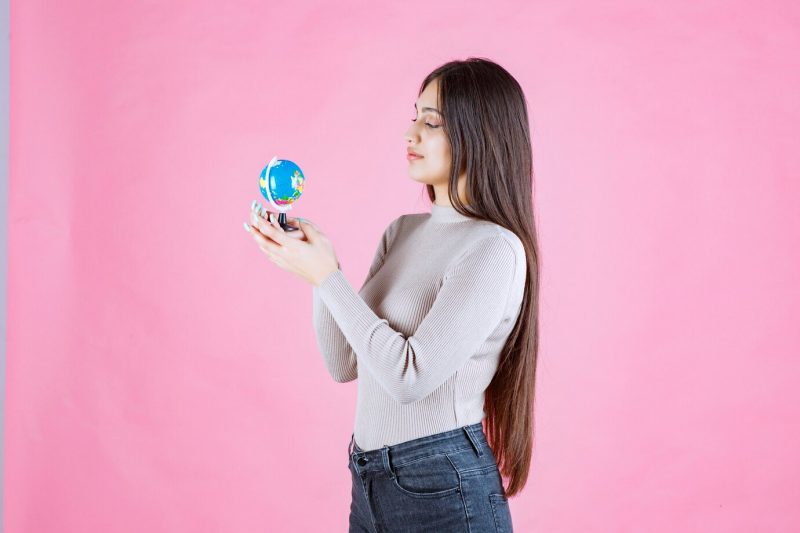 Girl holding a mini globe and studying it attentively Free Photo