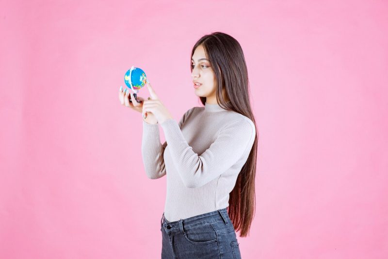 Girl holding a mini globe and studying it attentively Free Photo