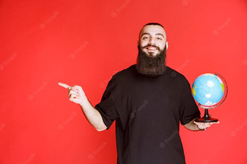 Man with beard holding a globe and pointing to somewhere. Free Photo