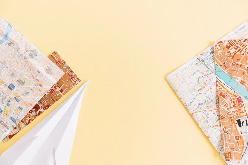 An overhead view of cities road maps and paper airplane on colored background Free Photo