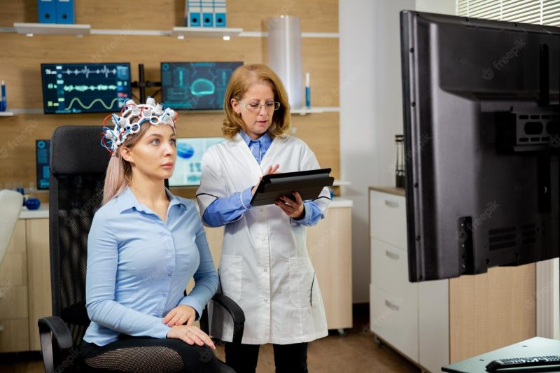 Patient woman scanning her brain and doctor making notes in the tablet holding it in her hand. brain waves scanning device Free Photo