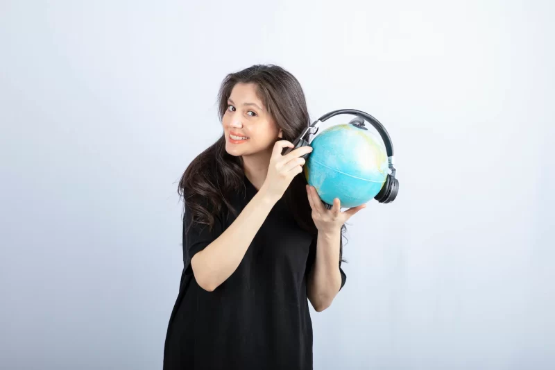 Smiling beautiful young woman standing and holding a globe in headphones . Free Photo