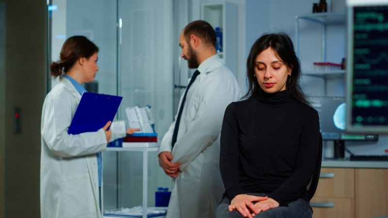 Team of scientists doctor discussing health status of patient, brain functions, nervous system, tomography scan while woman waiting for diagnosis of disease sitting in neurological research laboratory Free Photo