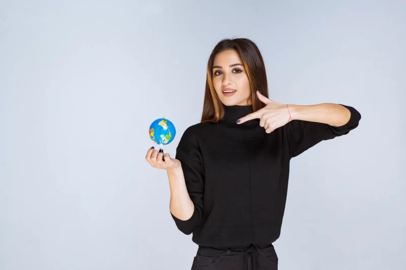 Woman holding a mini globe and finding locations on it. Free Photo